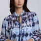 Woman wearing blue patterned blouse with ruffled collar and tie-neck detail