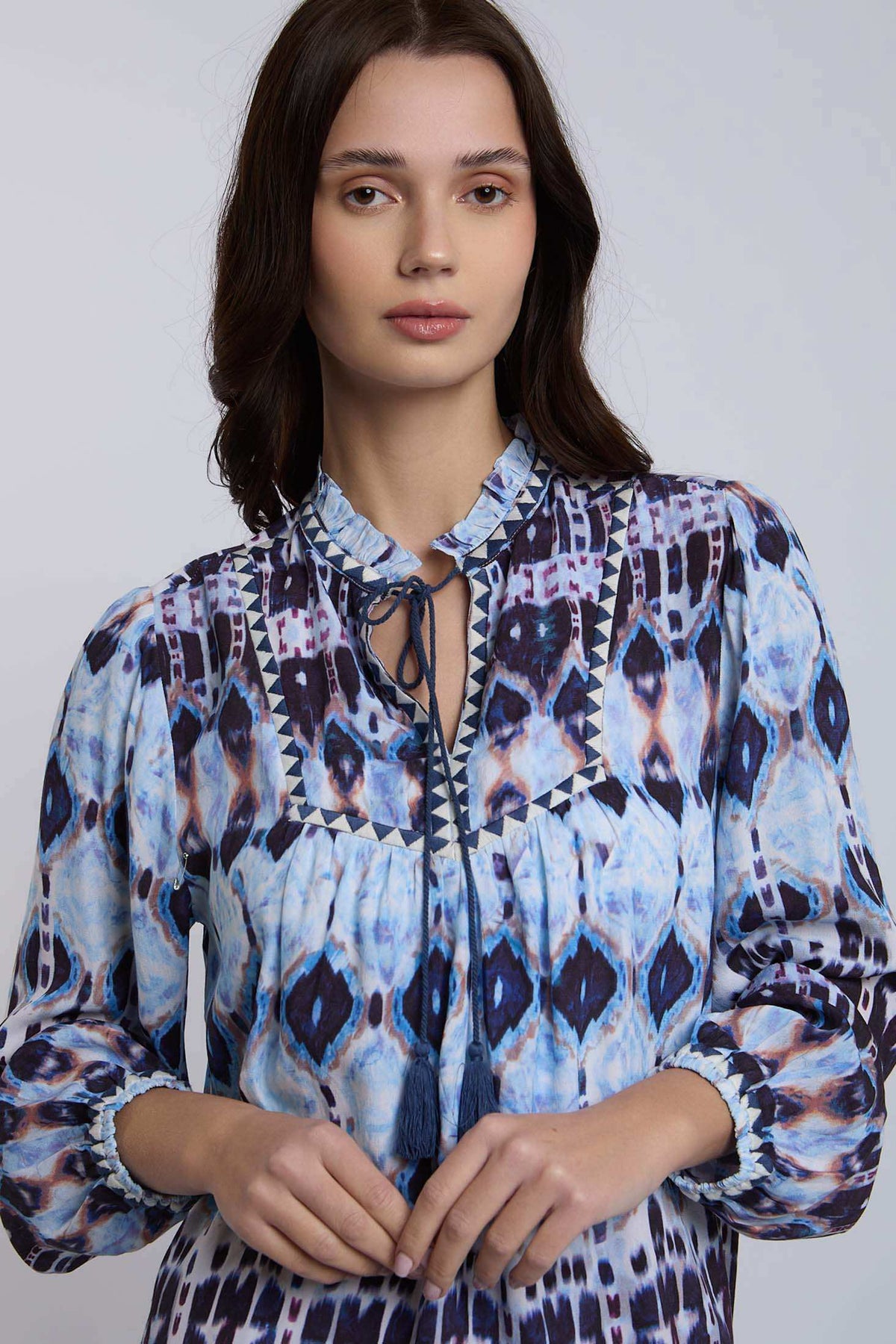 Woman wearing blue patterned blouse with ruffled collar and tie-neck detail