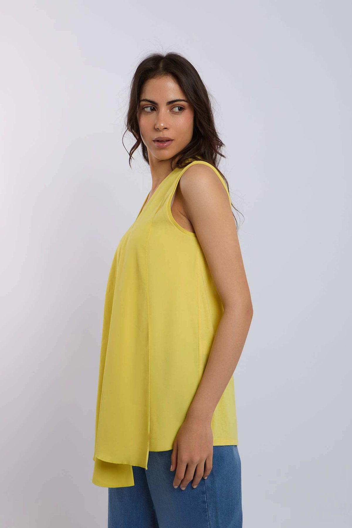Woman wearing sleeveless yellow top and blue jeans against plain background
