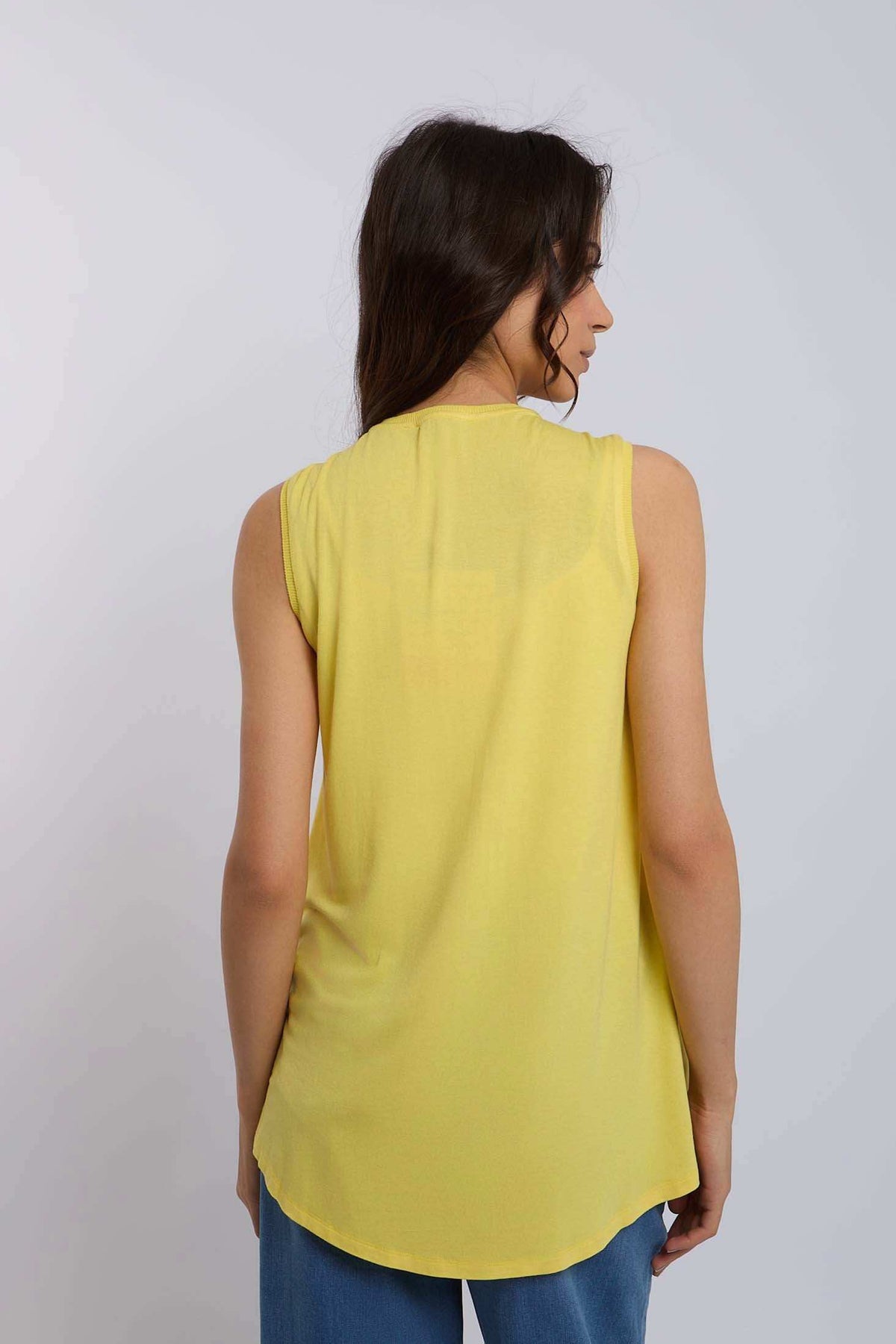 Woman wearing sleeveless yellow top and blue jeans, back view, casual fashion