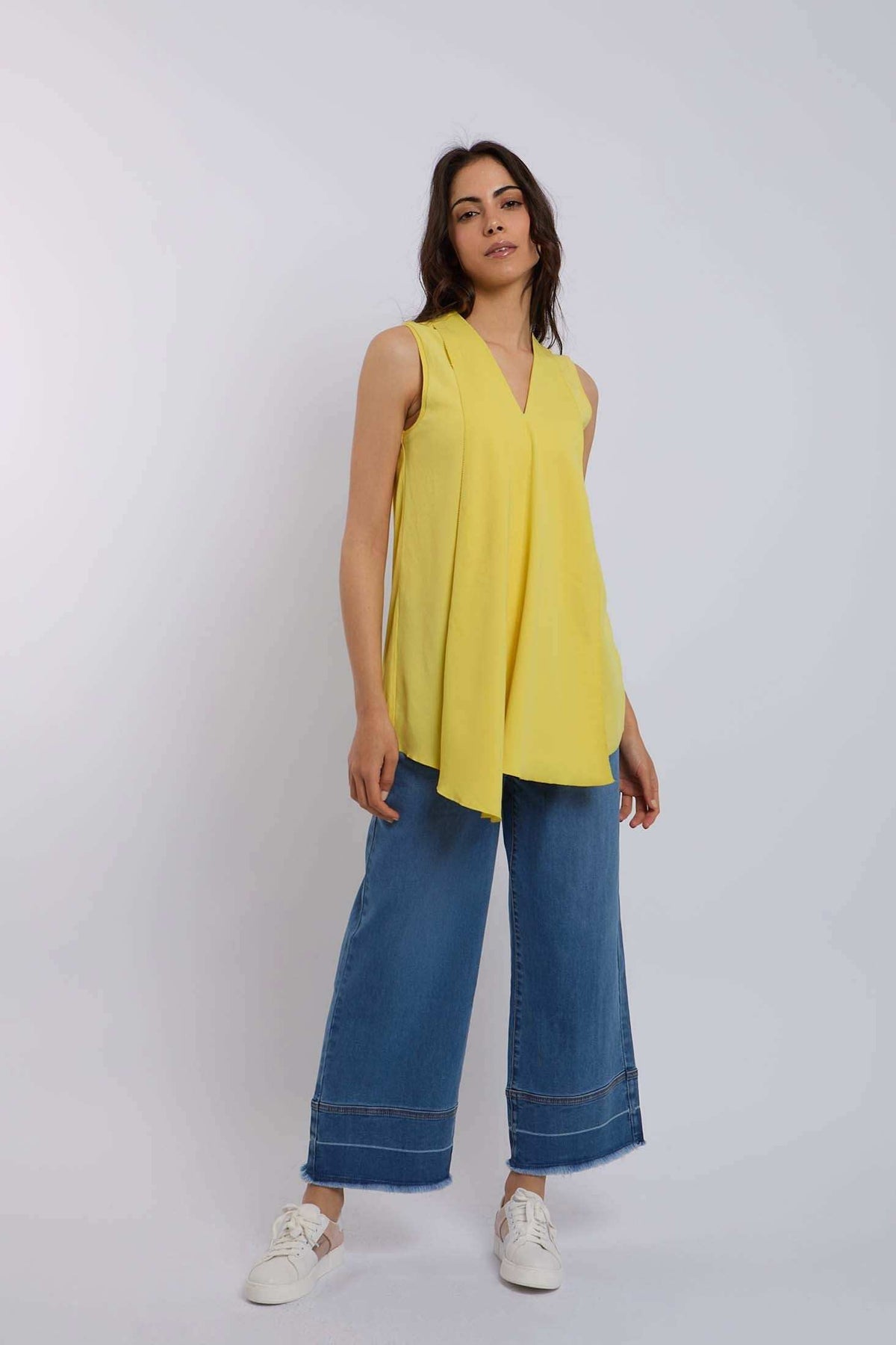 Woman wearing sleeveless yellow top with V-neck, wide leg blue jeans, and white sneakers