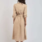 Woman in beige belted midi dress with rolled sleeves, standing against plain background