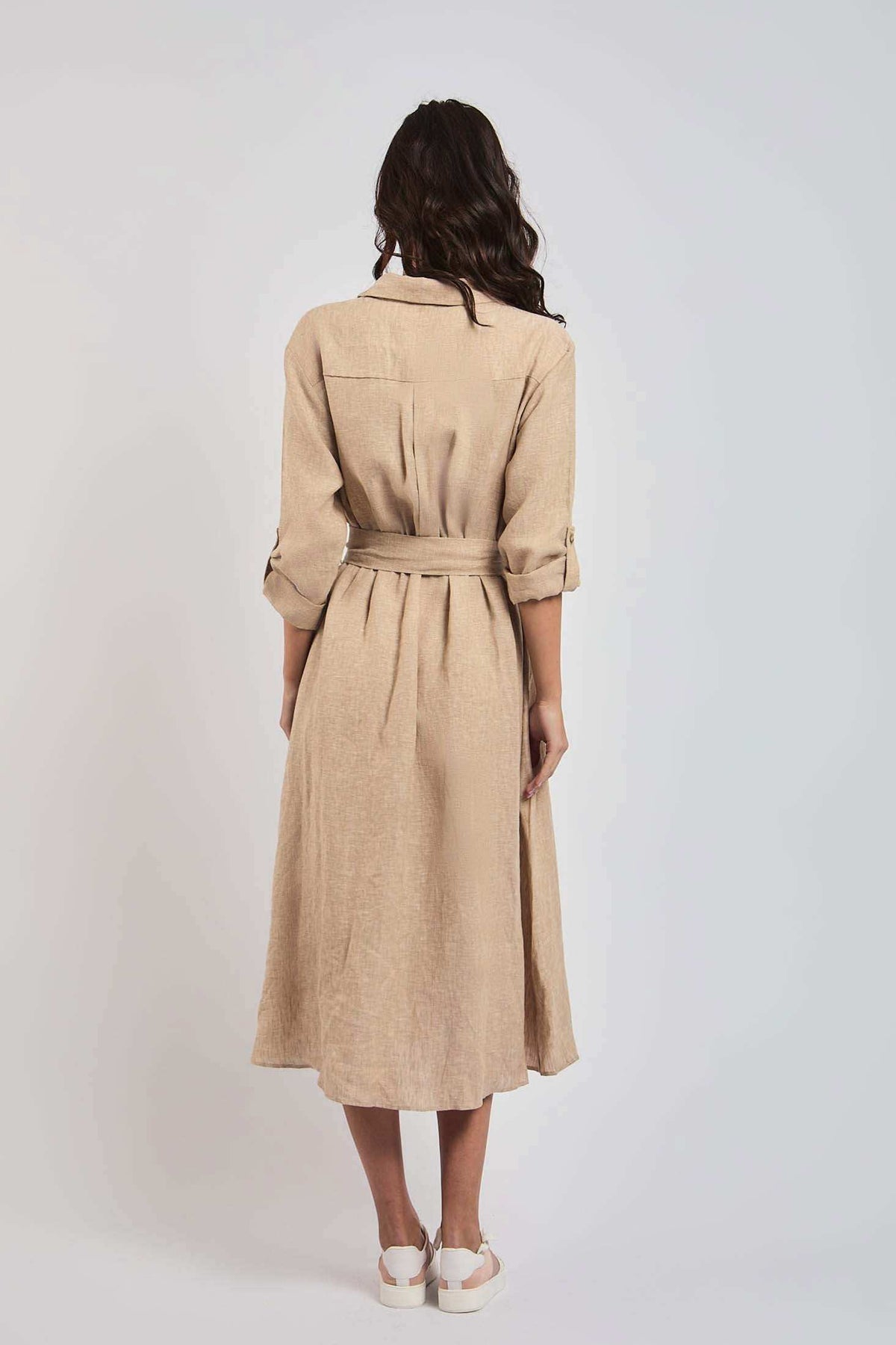 Woman in beige belted midi dress with rolled sleeves, standing against plain background