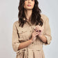 Woman wearing a beige belted shirt dress with pockets on a plain background