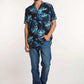 Man wearing a blue tropical print short sleeve shirt, blue jeans, and white sneakers