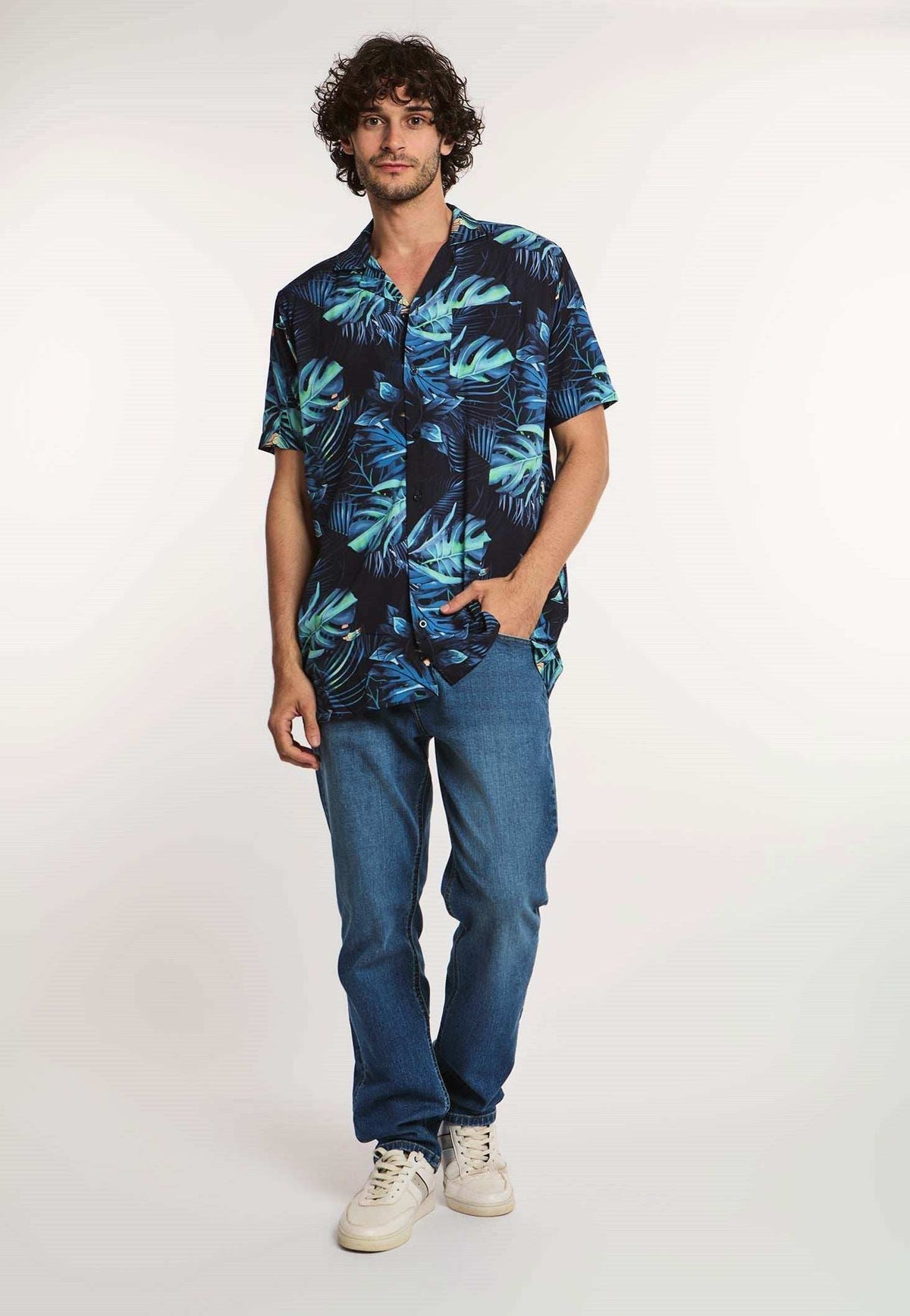 Man wearing a blue tropical print short sleeve shirt, blue jeans, and white sneakers
