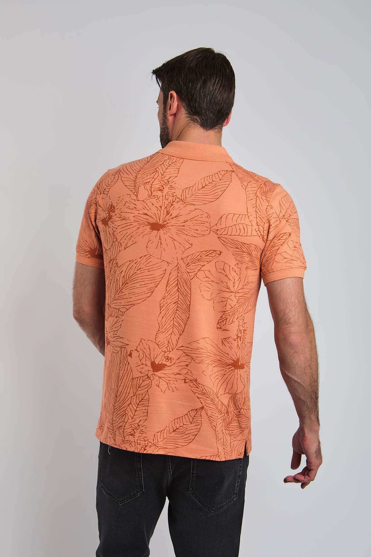 Back view of man in orange floral short sleeve polo shirt and dark jeans