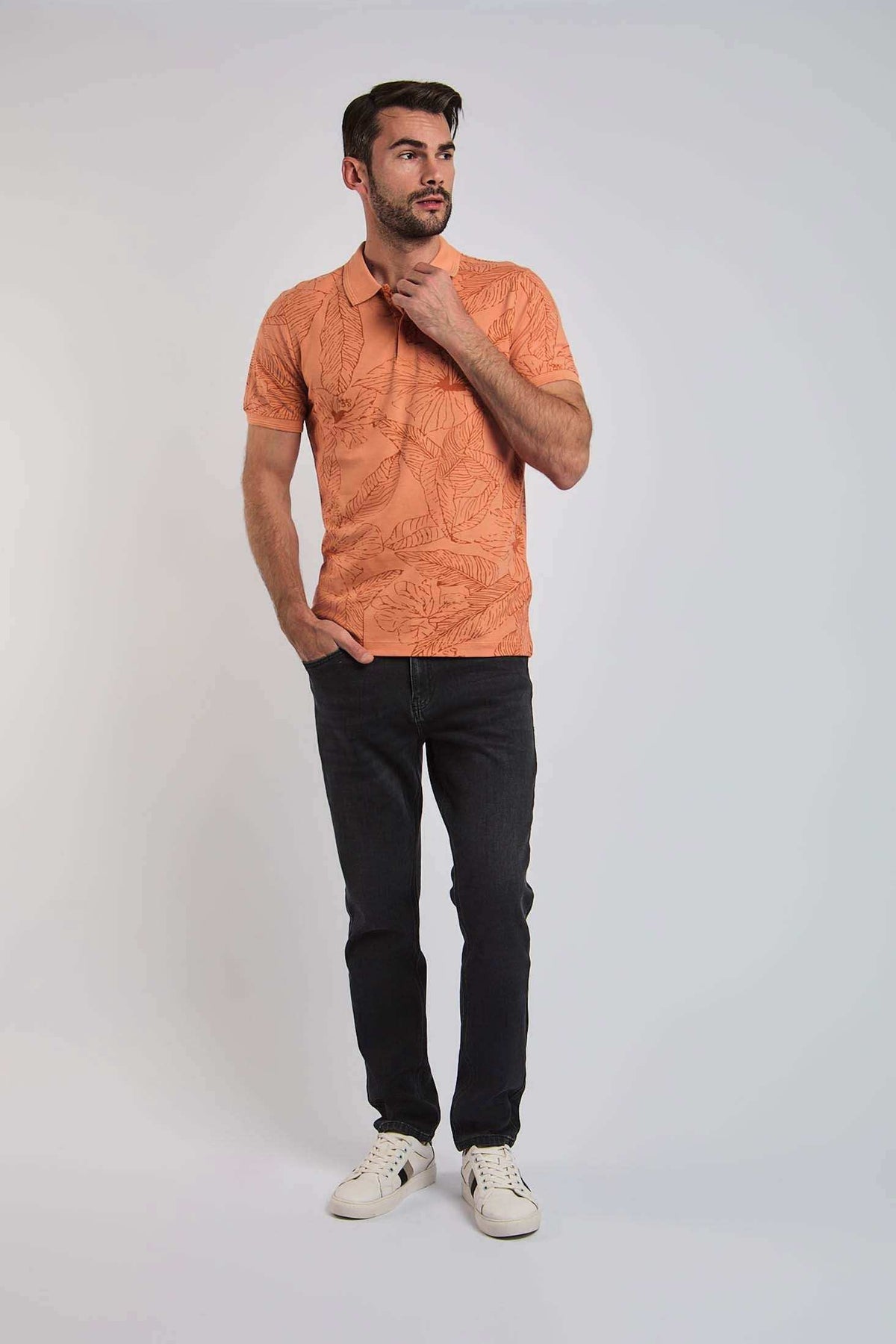 Man wearing an orange leaf-patterned polo shirt, black jeans, and white sneakers