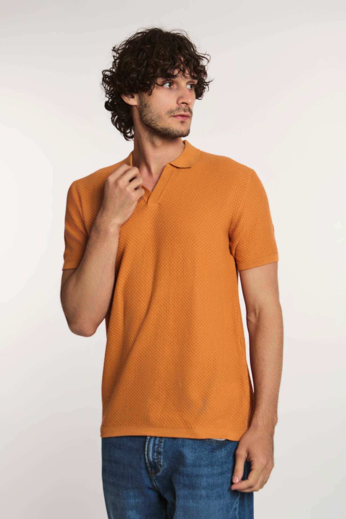 Man wearing textured orange polo shirt and blue jeans on white background
