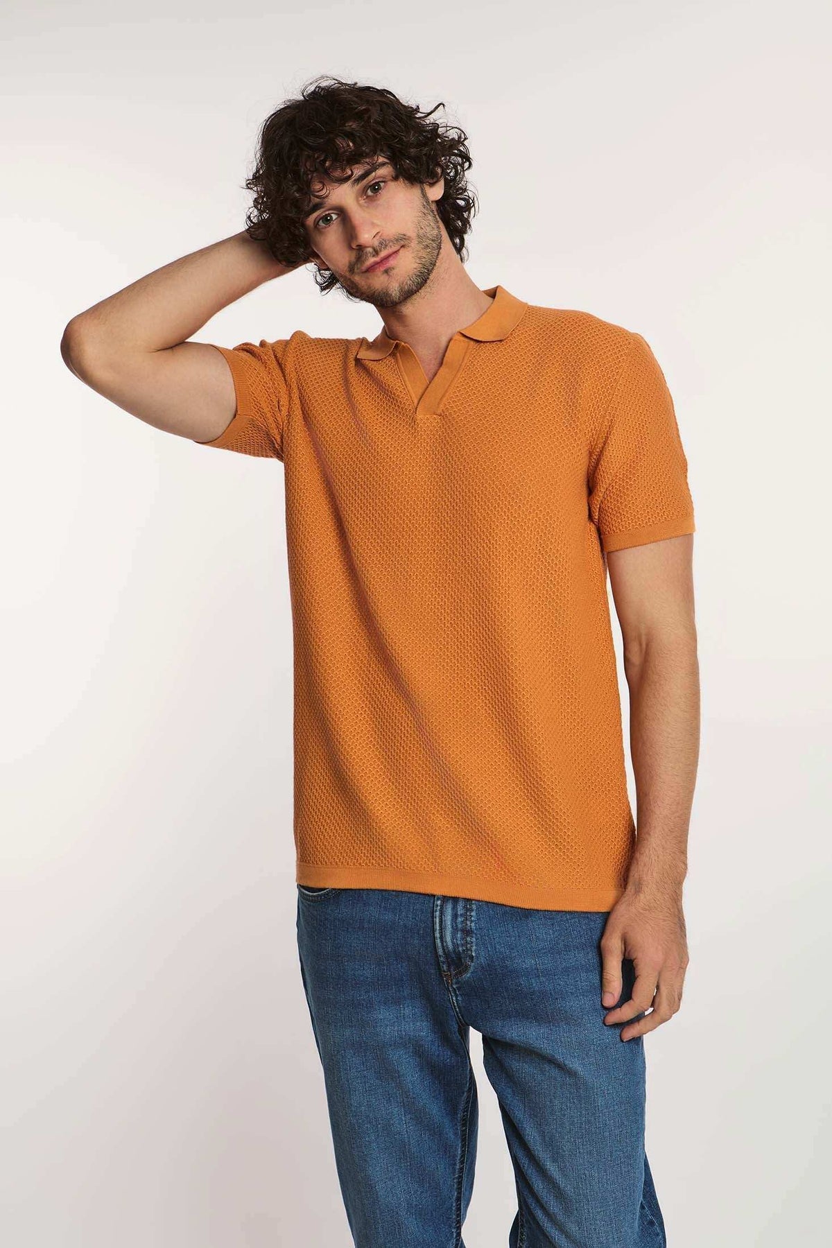 Man wearing short sleeve orange textured polo shirt and blue jeans on white background