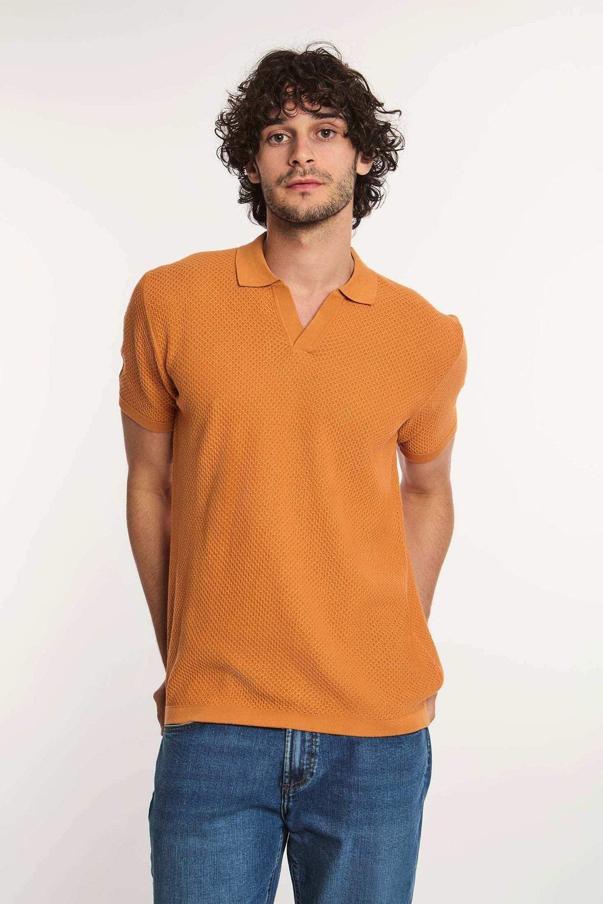 Man wearing textured orange short sleeve polo shirt and blue jeans against white background