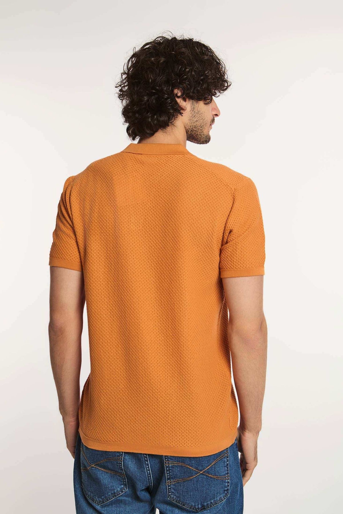 Man wearing textured orange short sleeve polo shirt and blue jeans, back view