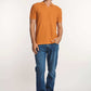 Man in an orange textured polo shirt, blue jeans, and white sneakers standing casually