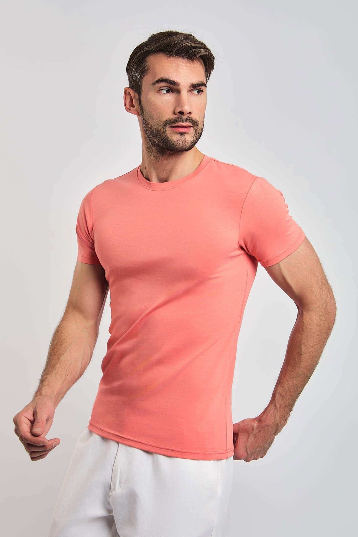 Man wearing fitted coral short-sleeve t-shirt and white pants on plain background