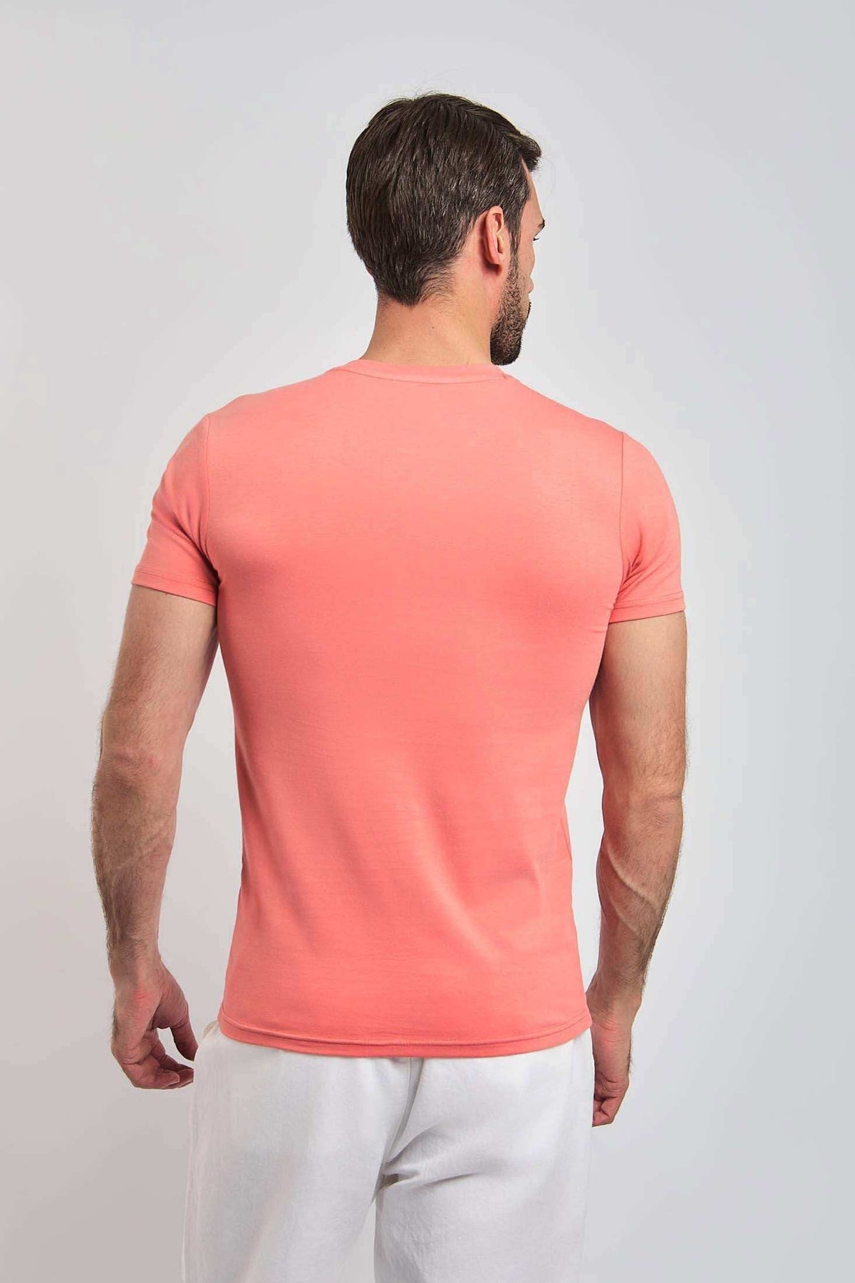 Man wearing coral short sleeve t-shirt and white pants, viewed from the back