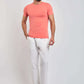 Man wearing a coral short-sleeve t-shirt, white pants, and white sneakers on plain background