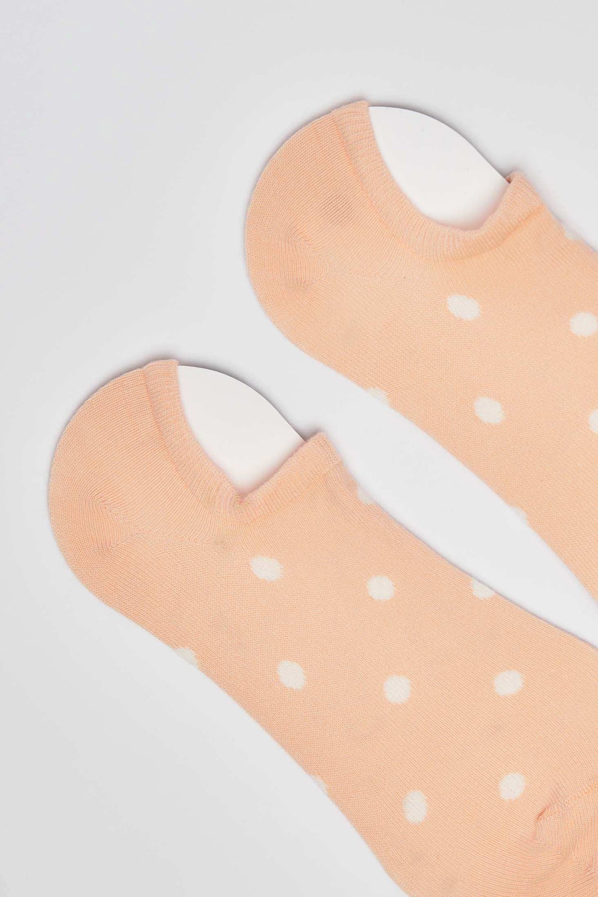 Peach low-cut socks with white polka dots on a plain background