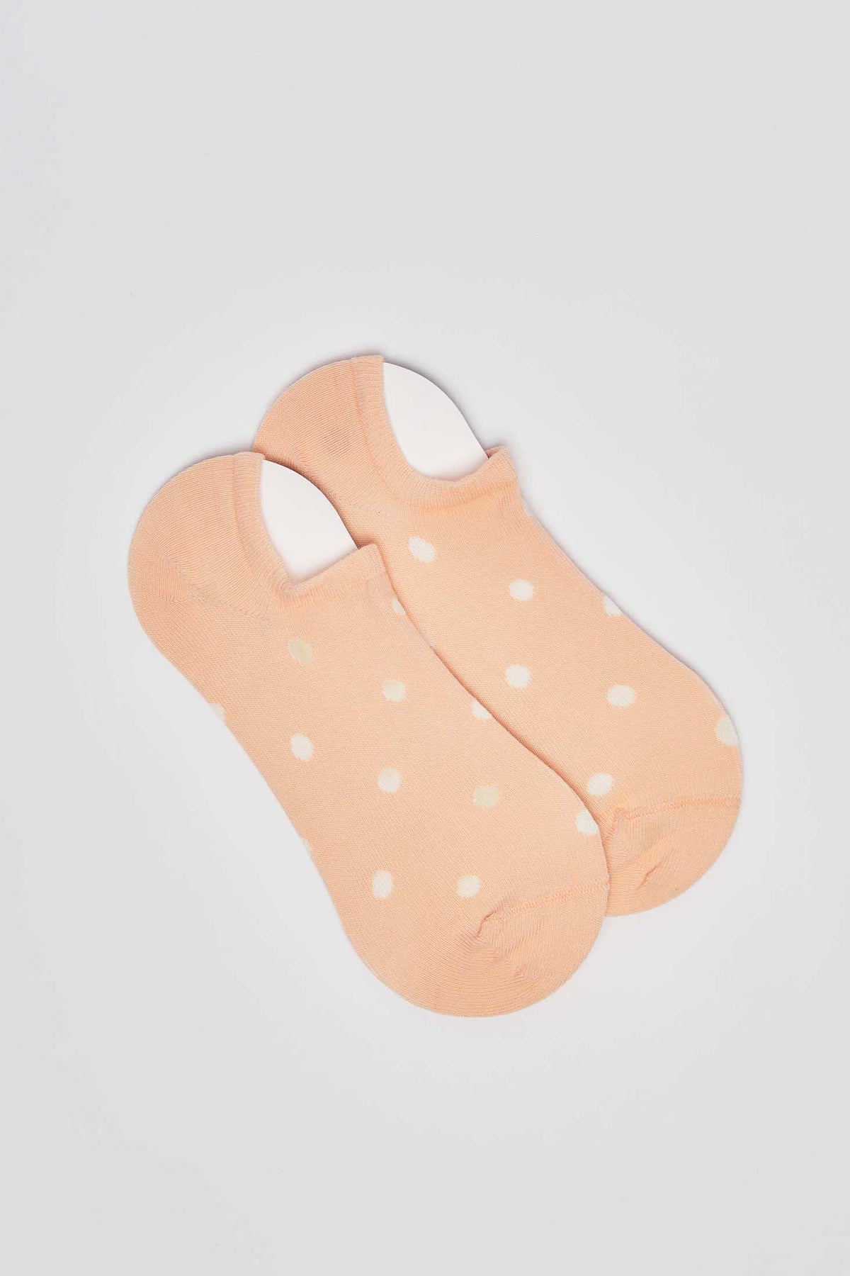 Peach ankle socks with white polka dots on a plain background