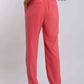Woman in coral pink high-waisted pants with back pockets and white blouse, back view