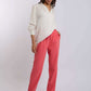 Woman wearing a white long sleeve blouse and coral pink pants, posing on a plain background