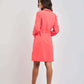 Woman in a bright coral long-sleeve dress with heels, standing against a plain background