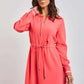 Woman in a coral pink long sleeve dress with waist tie and white cuff detail