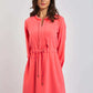 Woman wearing coral pink long sleeve casual dress with tie waist, standing against a plain background