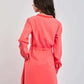 Woman wearing coral pink long sleeve dress, viewed from the back, against plain background