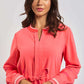 Woman wearing a coral long-sleeve dress with tie waist and white trim details.