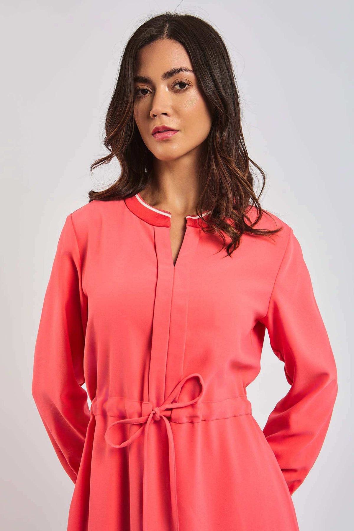 Woman in coral long sleeve dress with tie waist and white trim collar, urban casual style