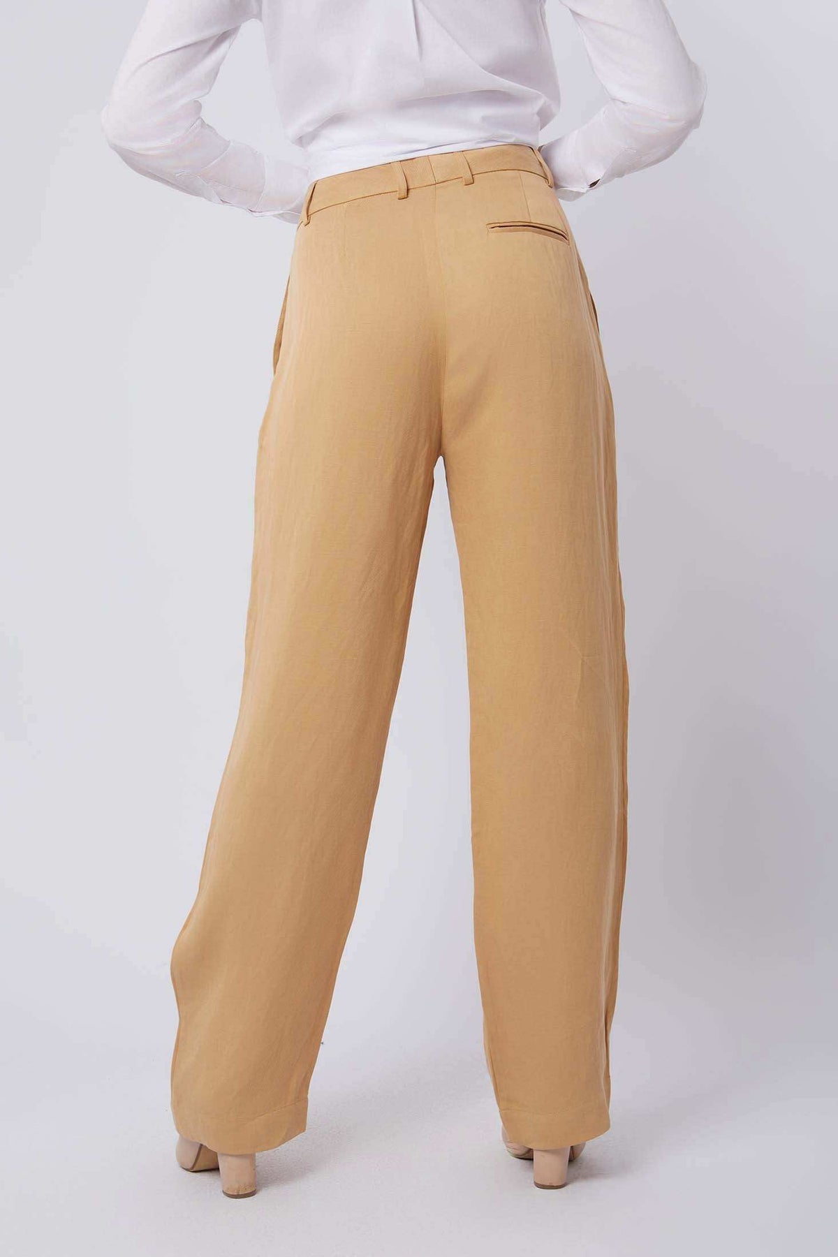 Back view of woman wearing high-waisted beige wide-leg trousers and white blouse