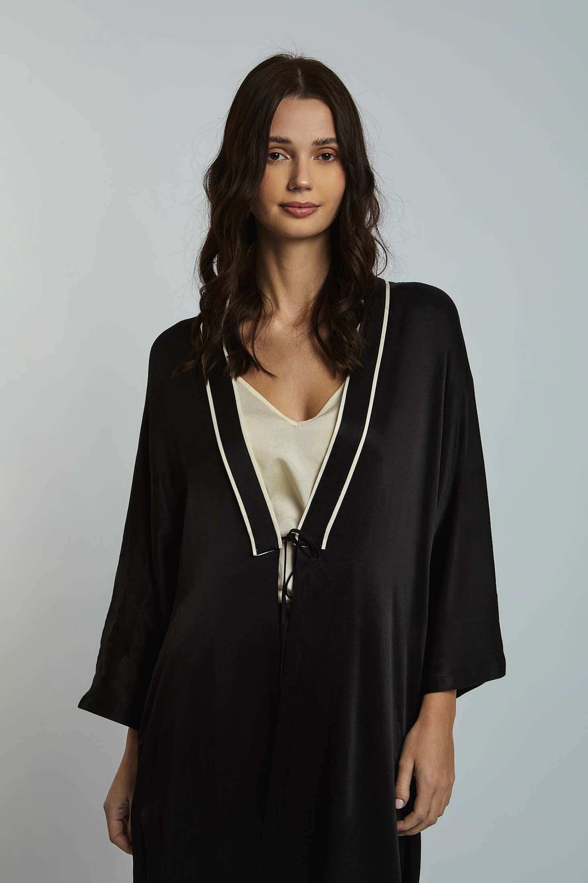 Woman wearing a black satin robe with white trim over a cream top, casual elegant fashion