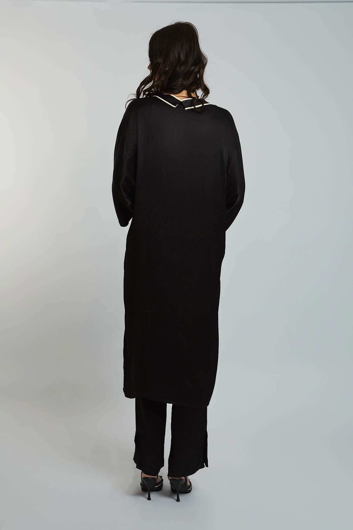 Woman in black long-sleeve tunic and pants set, back view, on plain background
