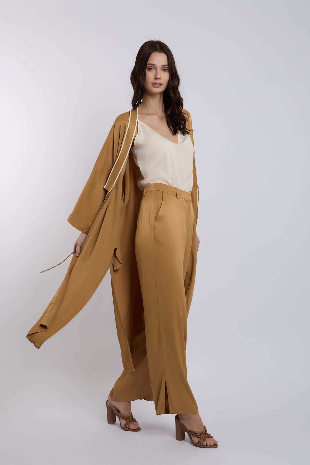 Woman wearing tan wide-leg pants, matching long coat, and cream blouse, fashion outfit