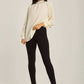 Woman wearing cream high neck blouse, black slim pants, and nude heels on neutral background