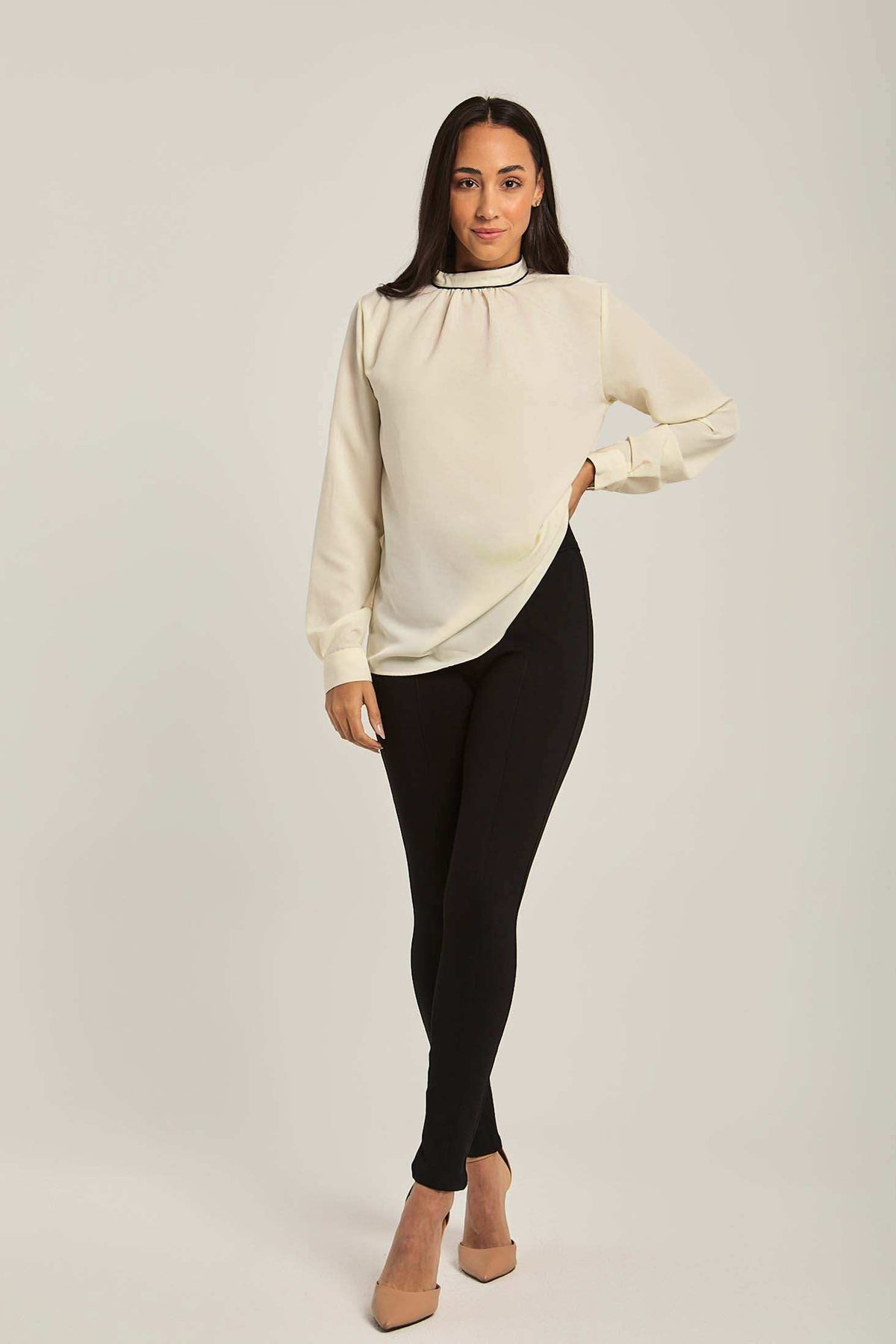 Woman modeling an off-white long sleeve blouse with black skinny pants and beige heels