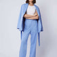 Woman wearing light blue pantsuit with blazer draped over shoulders and white top
