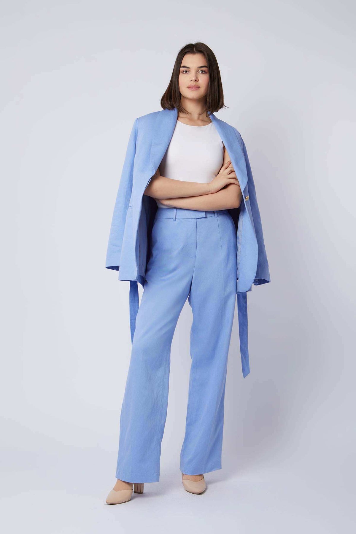 Woman wearing light blue pantsuit with blazer draped over shoulders and white top