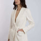 Woman wearing a white belted blazer with long sleeves and tailored fit