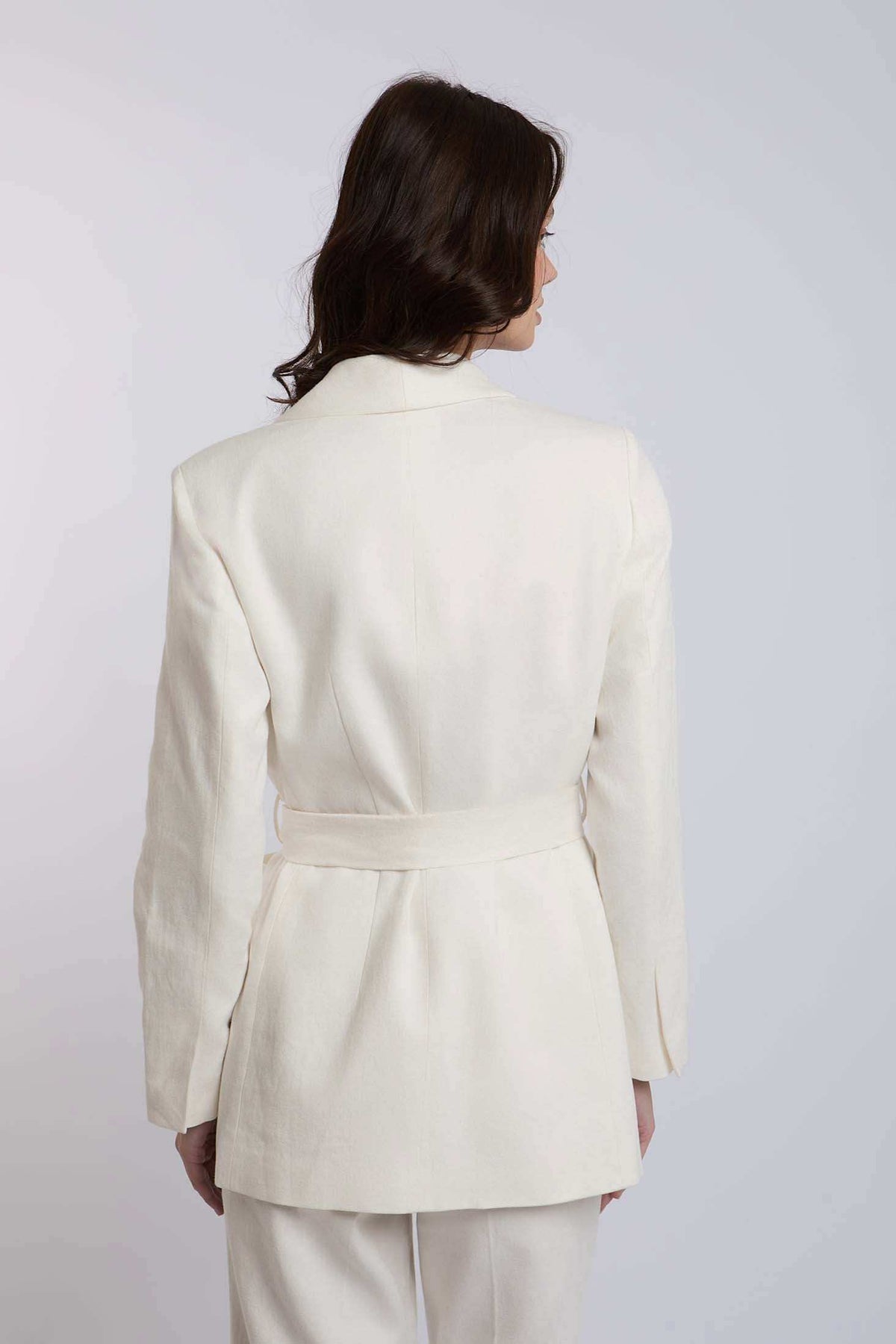 Woman wearing white belted blazer with long sleeves, back view, formal attire