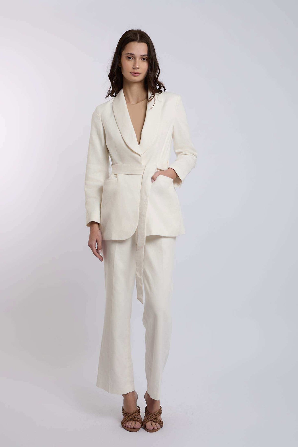 Woman wearing cream tailored linen blazer and wide-leg pants set on plain background